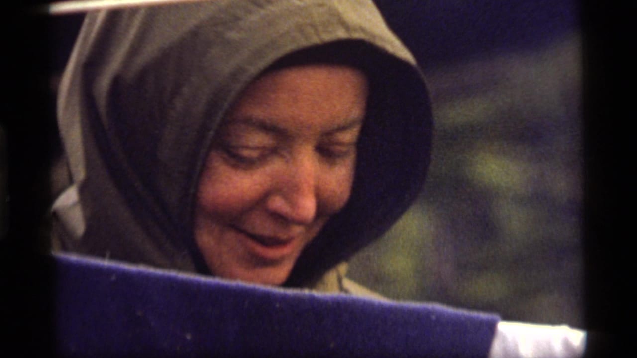 Woman in a gray hooded jacket smiles while looking down, with a dark foreground edge below her face.