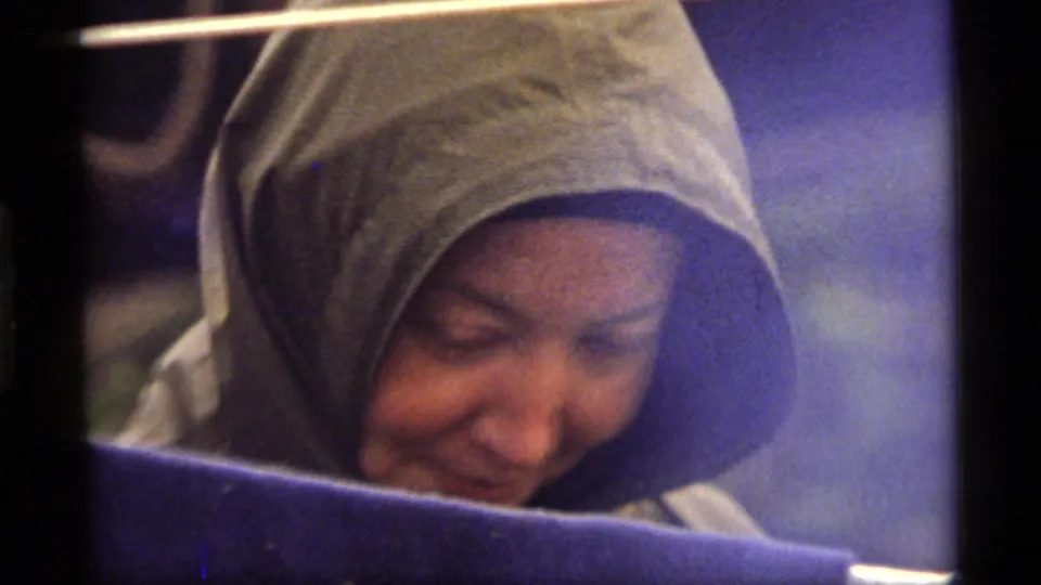 The hooded woman appears in another close 1977 Sapphire Lake frame, looking downward behind a dark foreground band.