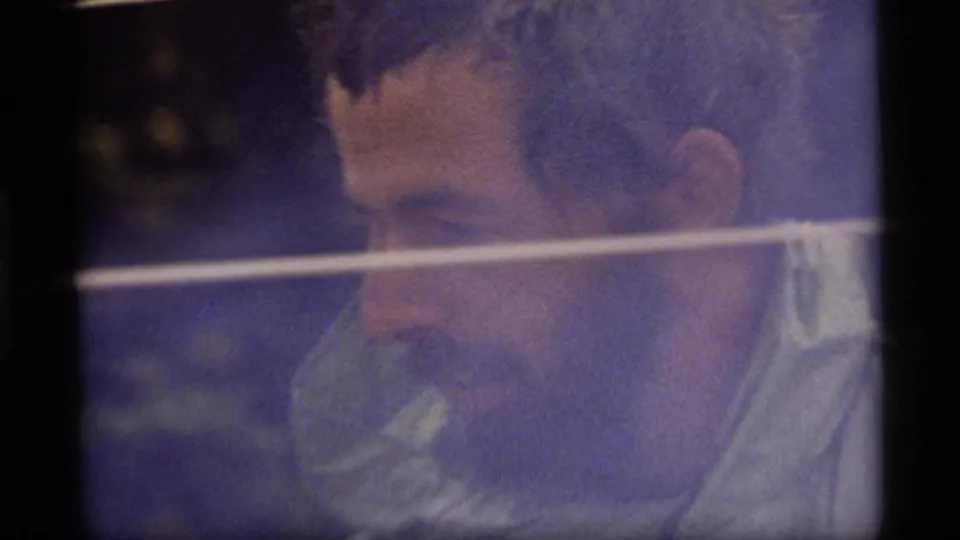 A bearded man in the 1977 Sapphire Lake home movie looks downward, partly softened by grain and blue-purple color drift.