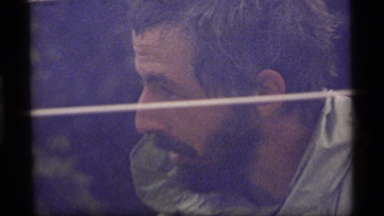 Bearded man in profile seen through dark frame edges with a pale horizontal line across the shot.