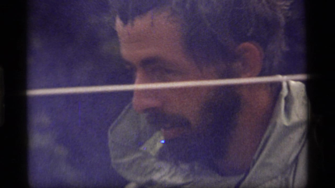 Close 1977 Sapphire Lake 8mm frame of a bearded man leaning forward outdoors, with soft focus, grain, and dark gate borders.