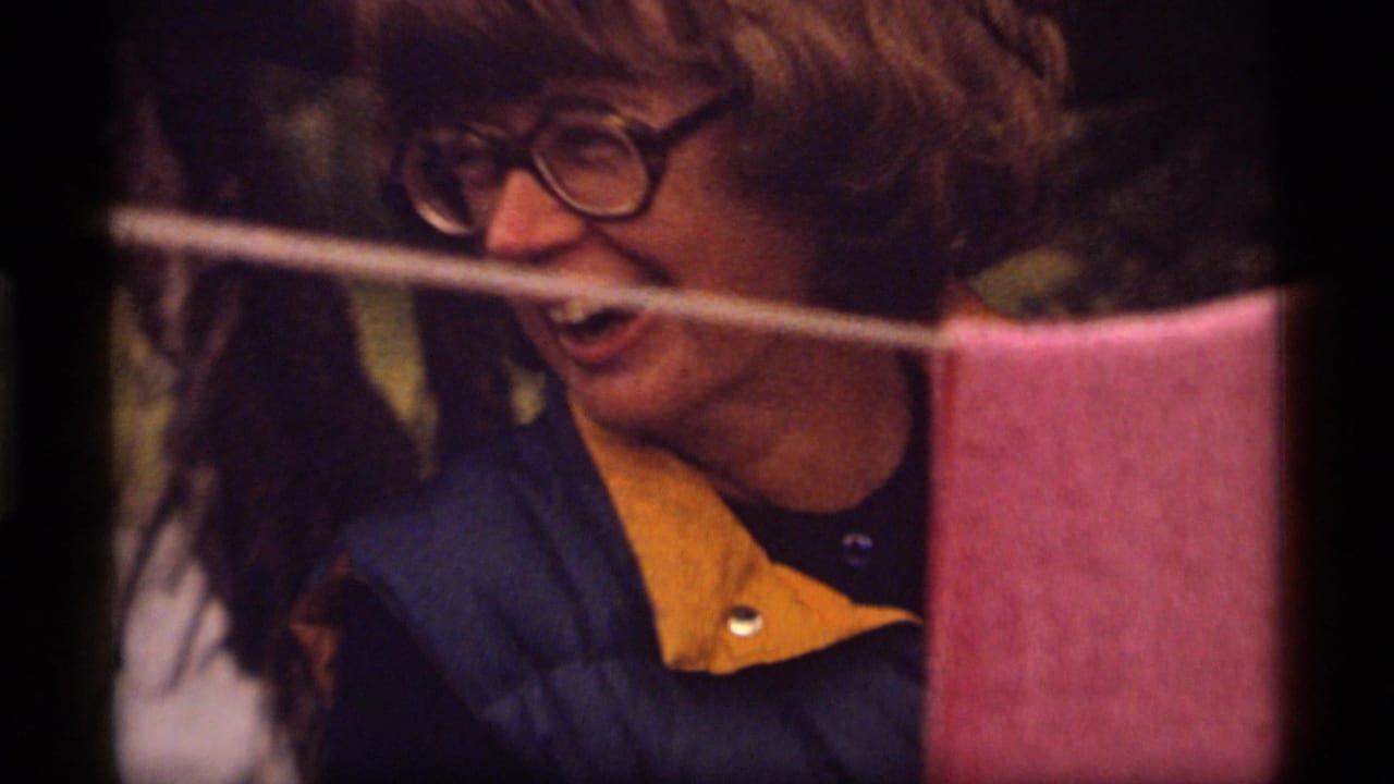 Woman in glasses smiles behind a clothesline with a pink towel.