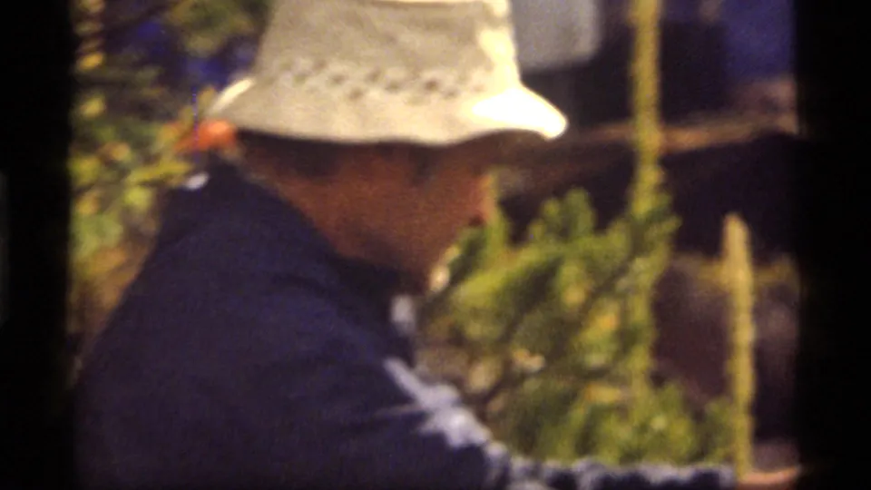 A soft-focus close view shows the man in a white hat and blue jacket against greenery in the 1977 Sapphire Lake footage.