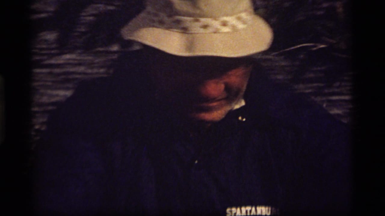 At Sapphire Lake, Montana in 1977, a man in a white bucket hat and dark jacket looks down in bright outdoor light.