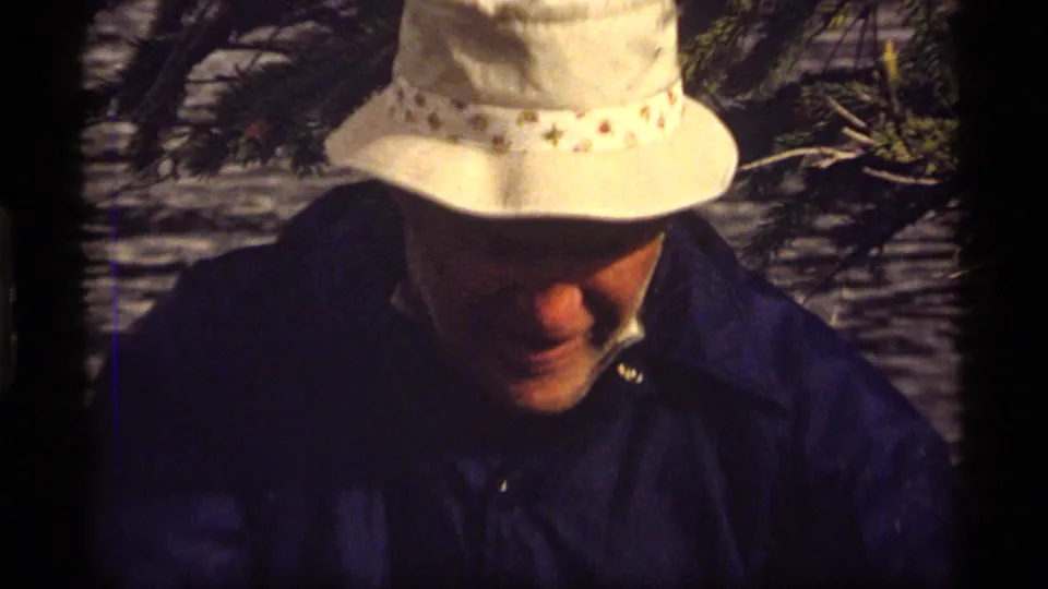 A close handheld 8mm frame shows the man looking down beneath a white hat near the Sapphire Lake shoreline.