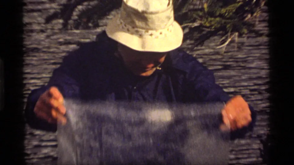 At Sapphire Lake, the man grips a reflective plastic sheet as it catches light and wind in the lakeside setting.