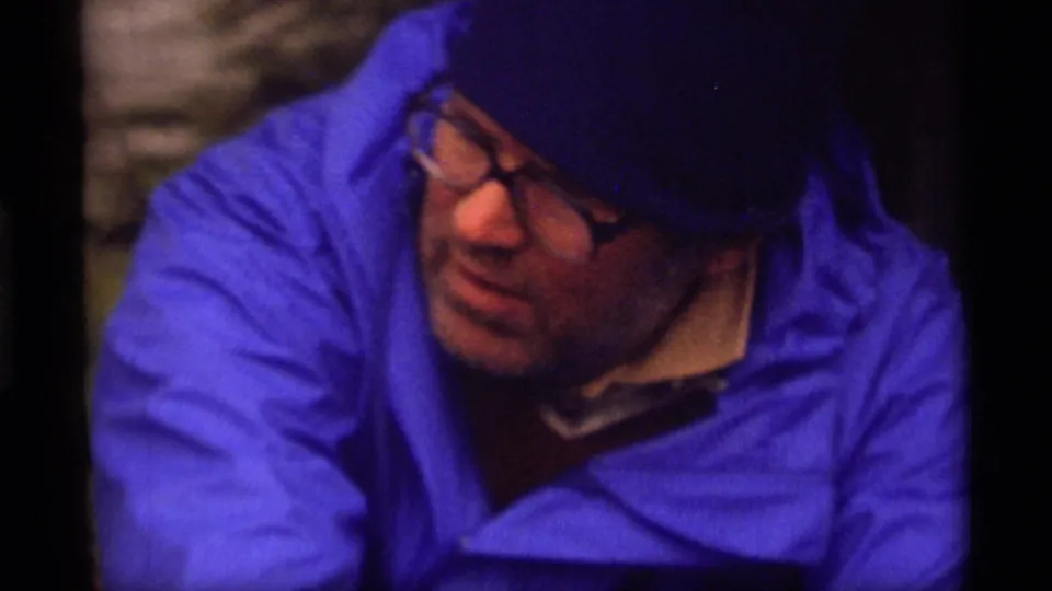 1977 Sapphire Lake home-movie frame showing the blue-jacketed camper turning to the side in soft, grainy 8mm footage.