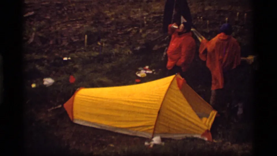 A yellow tent fills the foreground while two campers in orange jackets stand nearby in the Sapphire Lake, Montana campsite.