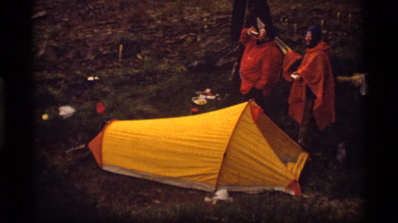 1977 Montana camping frame with two men in orange rain ponchos next to a yellow tent at Sapphire Lake.