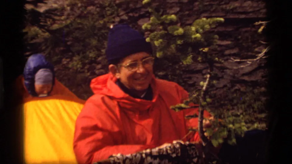 1977 Sapphire Lake camping frame with a smiling man in an orange poncho and another camper partly visible behind a yellow tent.