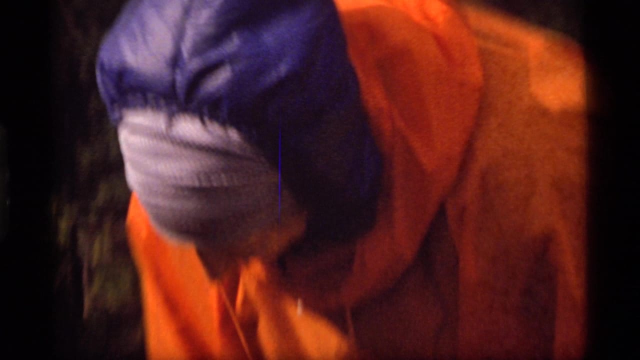 Close view of a person in an orange parka bending forward outdoors.