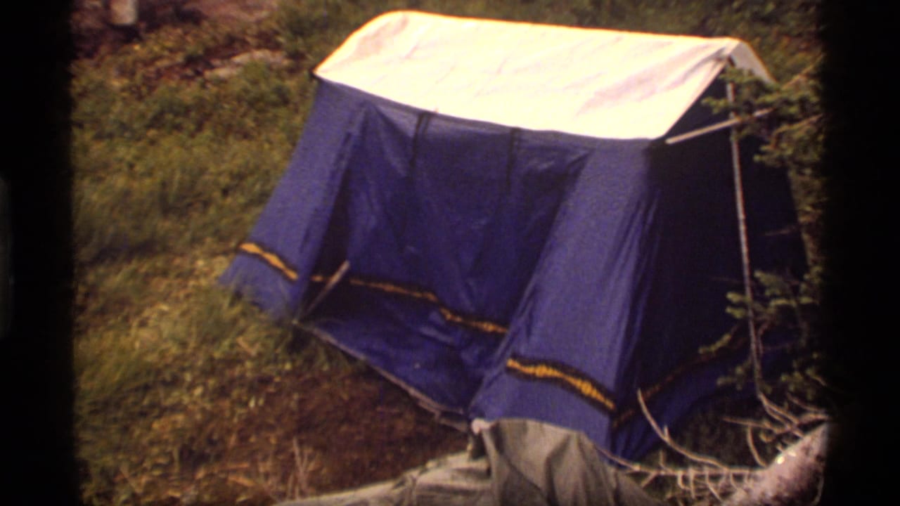 1977 Sapphire Lake, Montana home-movie frame showing a blue tent with yellow trim on grass among trees and brush.