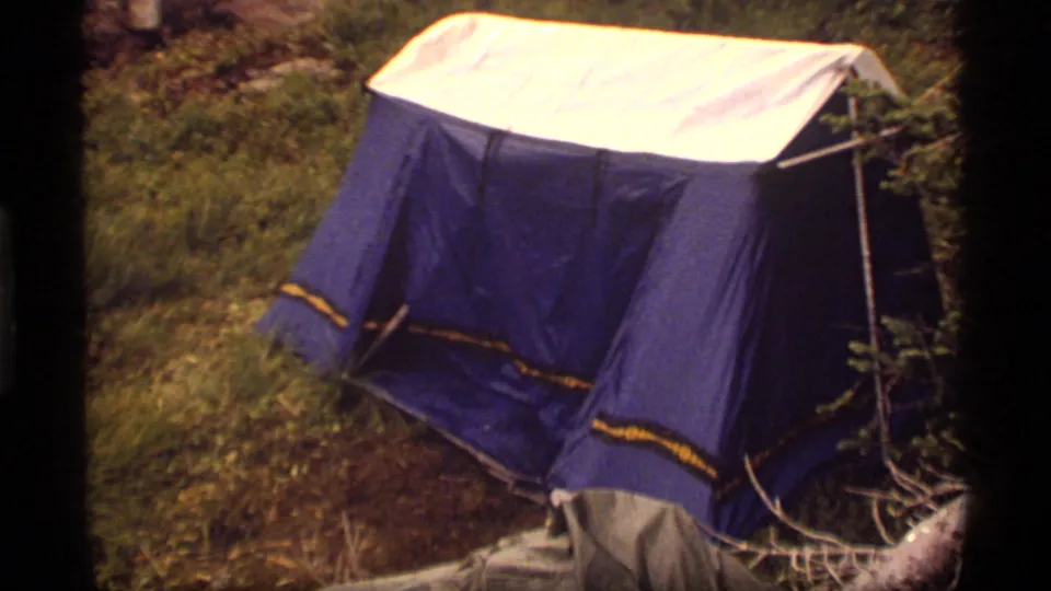 1977 Sapphire Lake, Montana home-movie frame showing a blue tent with yellow trim on grass among trees and brush.