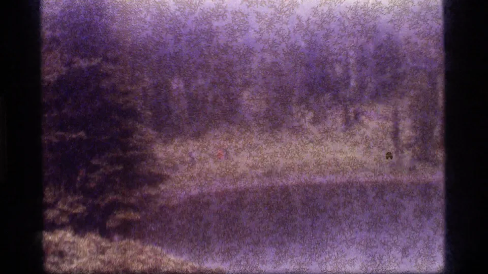 Soft, purple-cast 8mm view of Sapphire Lake with a distant shoreline walker, trees and reflective water.