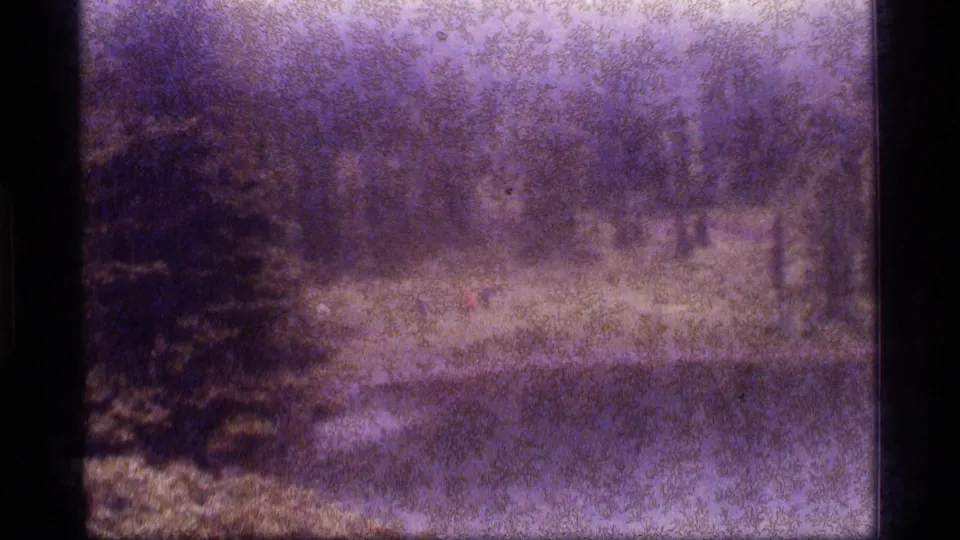 Grainy 8mm frame of Sapphire Lake with a distant hiker on the shore, evergreen trees and a calm lake surface.
