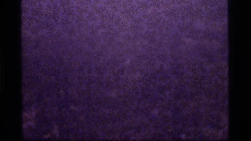 1977 8mm frame showing a darker purple-blue abstract field with dense grain, uneven exposure, and a black vertical film border.