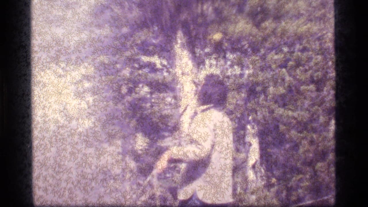 Side view of a man in 1977 Sapphire Lake forest footage as he works with rope beneath dense tree cover.