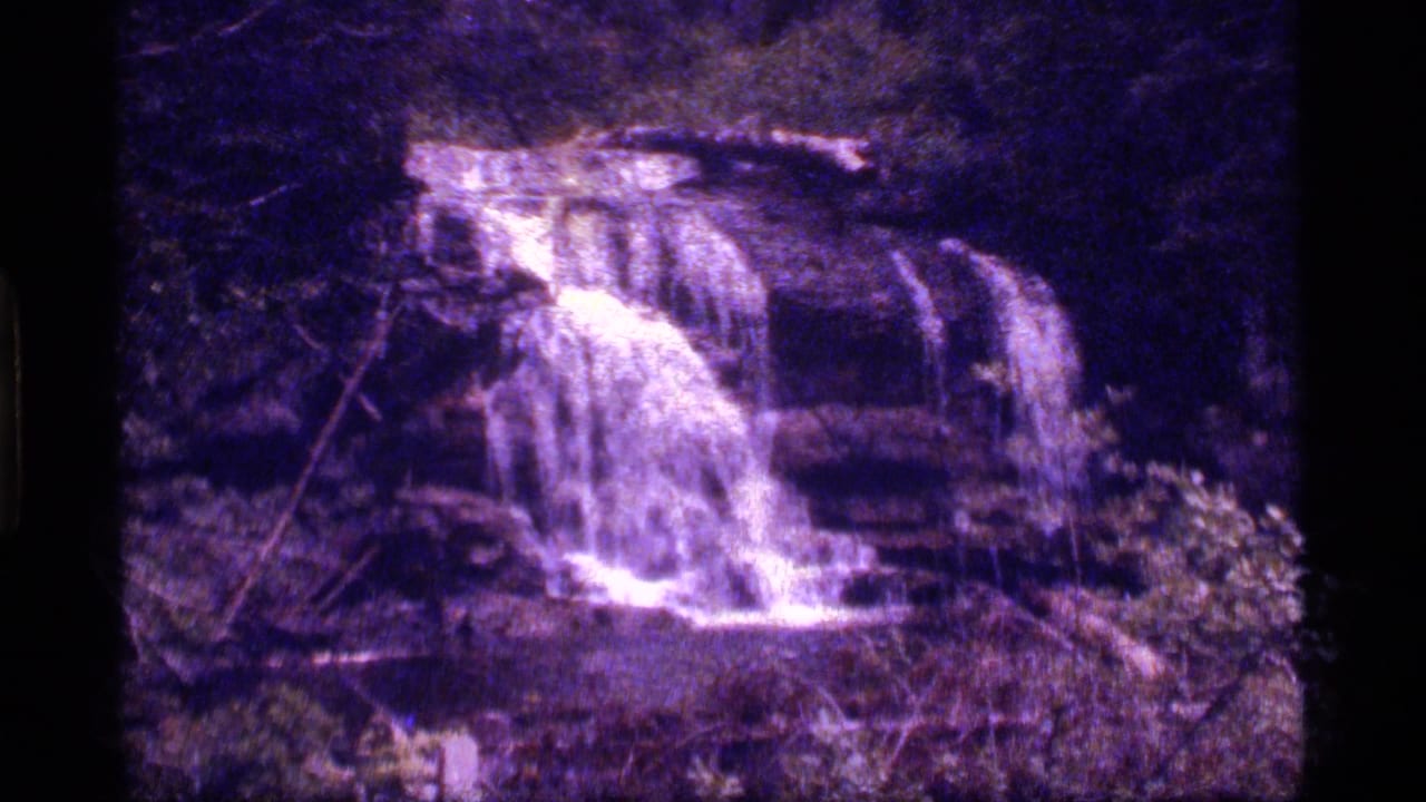 Small waterfall cascading over rocky ledges in a dark forest setting.