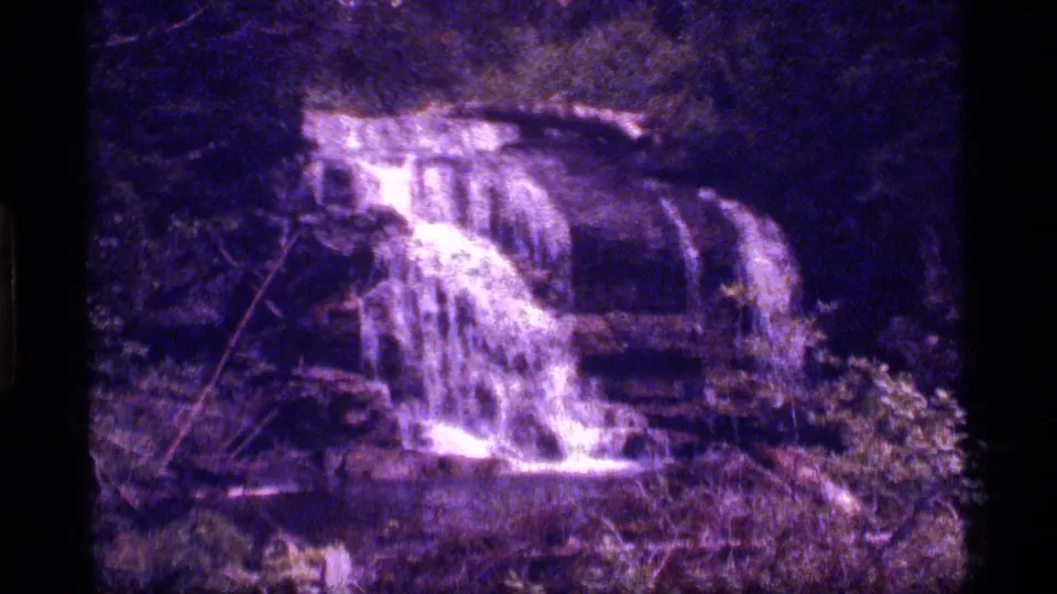 A closer 8mm frame shows the forest waterfall running over uneven rock shelves, with heavy grain and a pronounced purple cast.