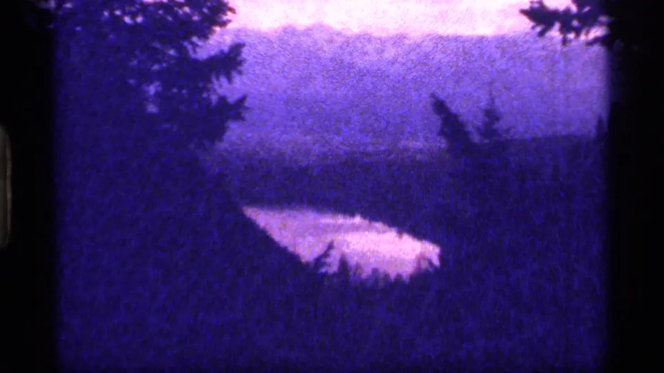 A slightly shifted 8mm view shows Sapphire Lake through foreground evergreens, with pale water and a dark wooded hillside beyond.