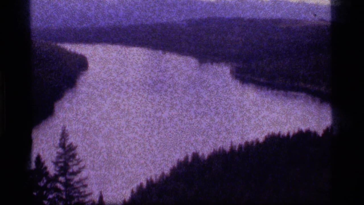 Winding pale water surface with dark wooded shoreline and distant hills.