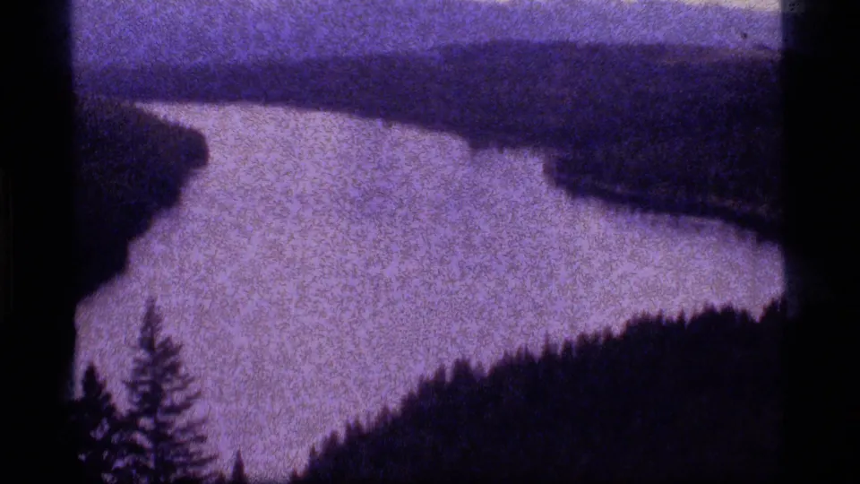 Sapphire Lake area landscape view with a pale winding water surface, dark tree-covered banks, and visible 8mm grain.