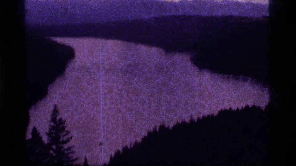 Dark 8mm view of the Sapphire Lake area with water bordered by forest, pine silhouettes, and visible film wear.
