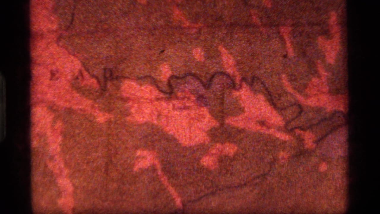 1977 8mm frame from Sapphire Lake, Montana showing a red-tinted topographical map with grain, scratches, and dark gate edges.