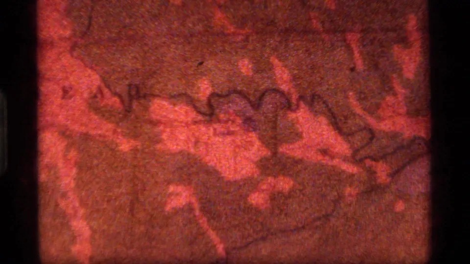 1977 8mm frame from Sapphire Lake, Montana showing a red-tinted topographical map with grain, scratches, and dark gate edges.