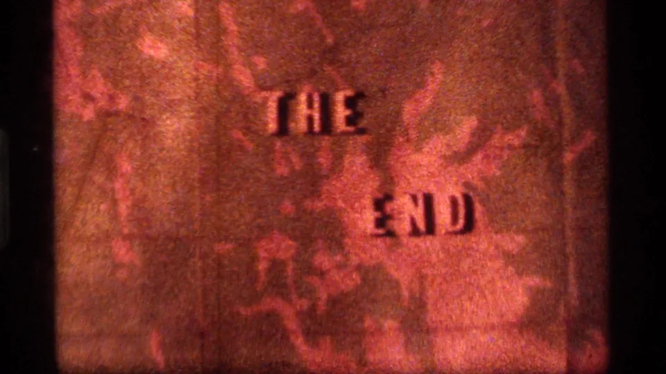 Final 1977 8mm frame showing THE END on a red topographical map, with grain, scratches, and black film borders.