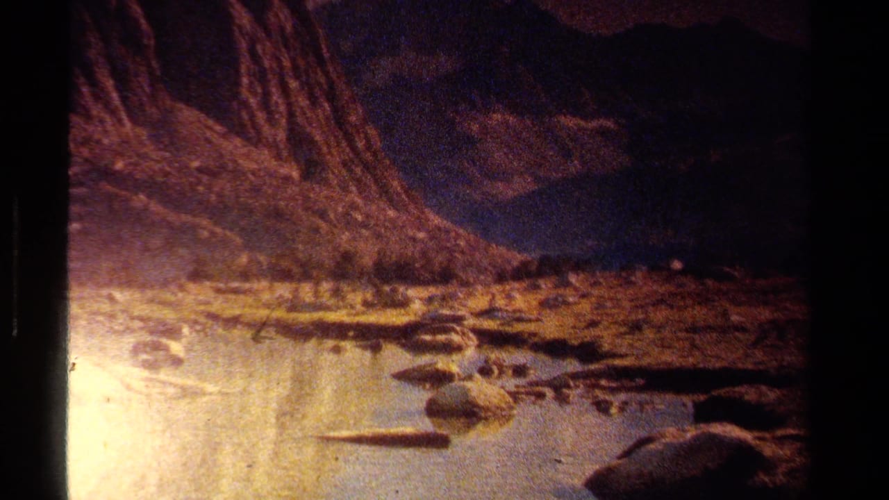 Rocky stream or shoreline under dark slopes with warm exposure on grainy film.