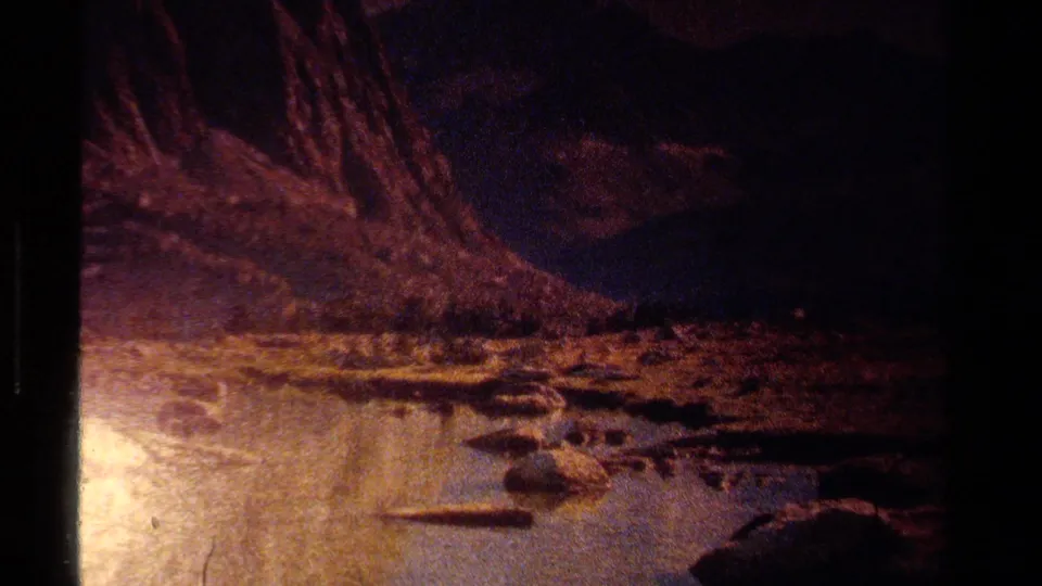 Dark 1978 Lake Tahoe 8mm frame showing a rocky water edge and mountain terrain, with most detail falling into deep shadow.