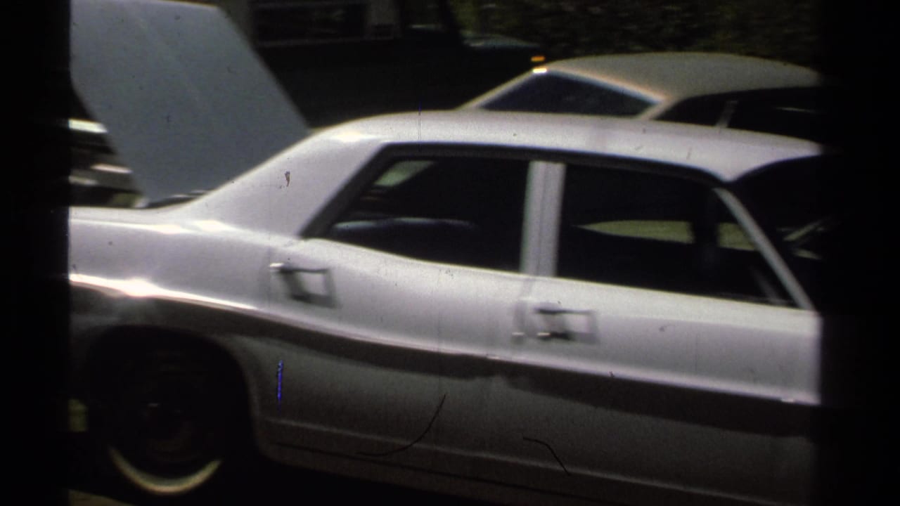 Side view of a white sedan with the hood open, with another light-colored car behind it in a 1978 roadside setting.