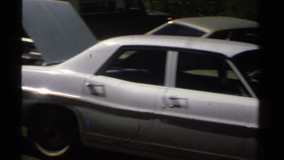 Side view of a white sedan with the hood open, with another light-colored car behind it in a 1978 roadside setting.