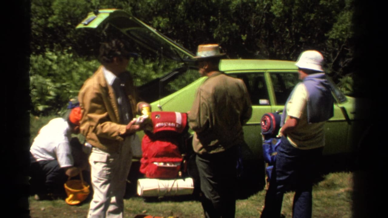 Adults in hats and casual outdoor clothing stand by a green hatchback with backpacks and rolled mats at Lake Tahoe in 1978.