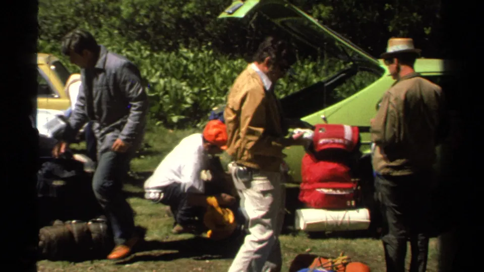 A 1978 Lake Tahoe home-movie frame shows hikers handling packs and bags beside a green car in a wooded outdoor area.