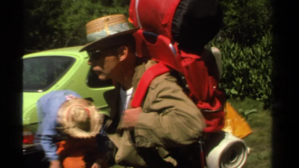 1978 Lake Tahoe frame with a man in a straw hat carrying a large red backpack while others pack gear nearby.
