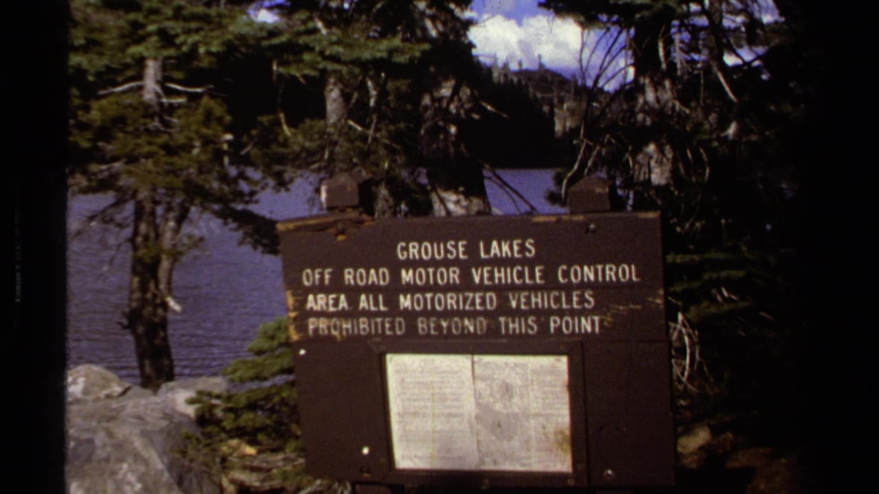 1978 8mm Lake Tahoe-area frame showing a Grouse Lakes off-road motor vehicle control sign near pine trees and lake water.