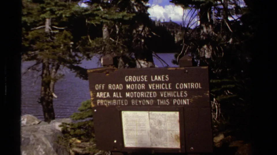 1978 8mm Lake Tahoe-area frame showing a Grouse Lakes off-road motor vehicle control sign near pine trees and lake water.