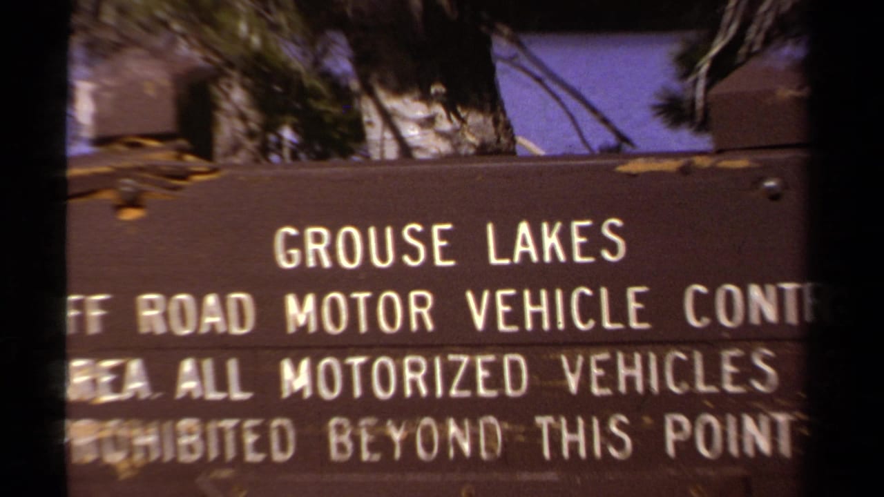 Close view of the Grouse Lakes sign text with trees and sky behind it.