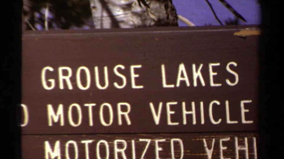 Tight 8mm frame of the Grouse Lakes sign, showing enlarged white lettering and partial off-road motor vehicle restriction text.