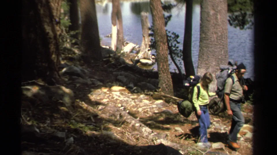 The man and woman appear to pause or adjust their steps on the rocky Lake Tahoe trail, framed by tree trunks and dappled light.
