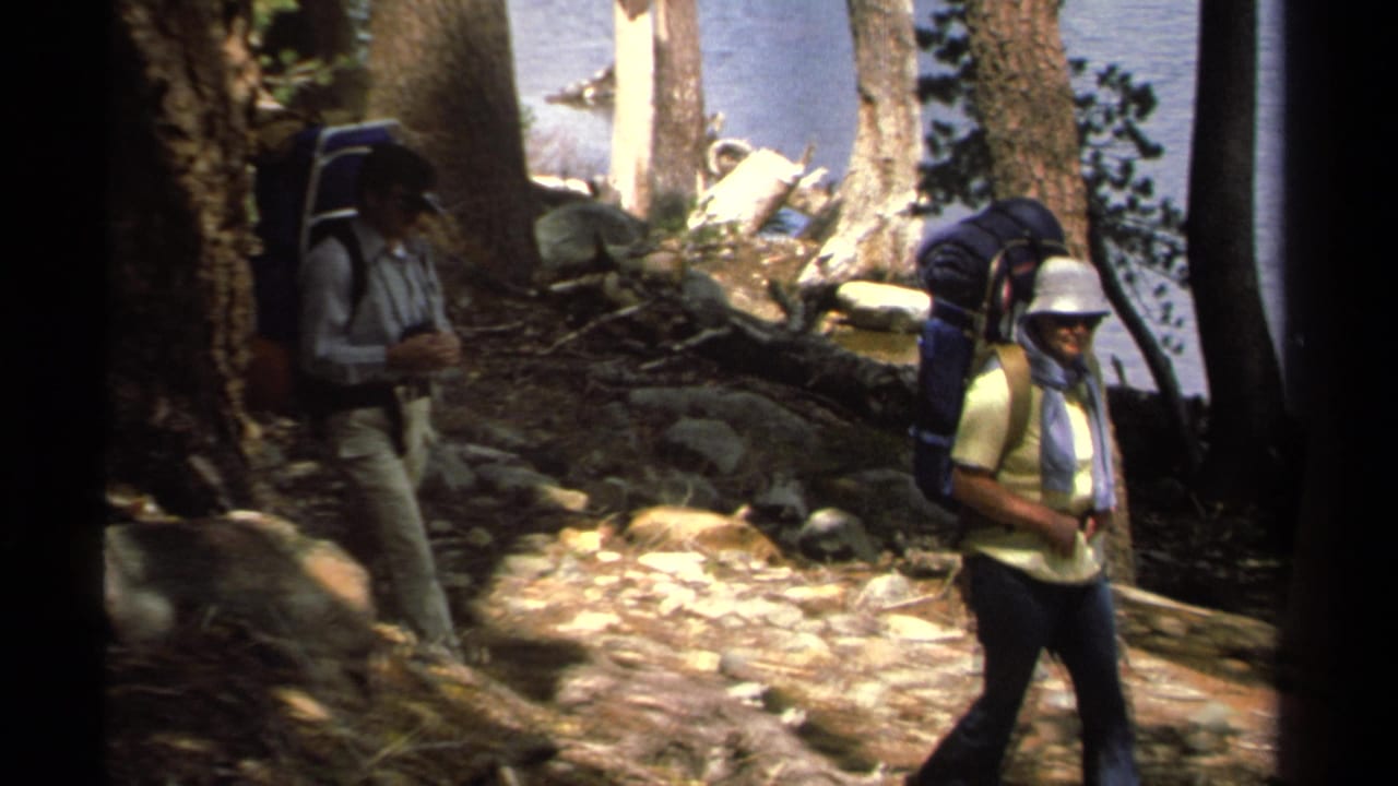 Two hikers with large backpacks move along a rocky wooded trail near Lake Tahoe in 1978 home-movie footage.