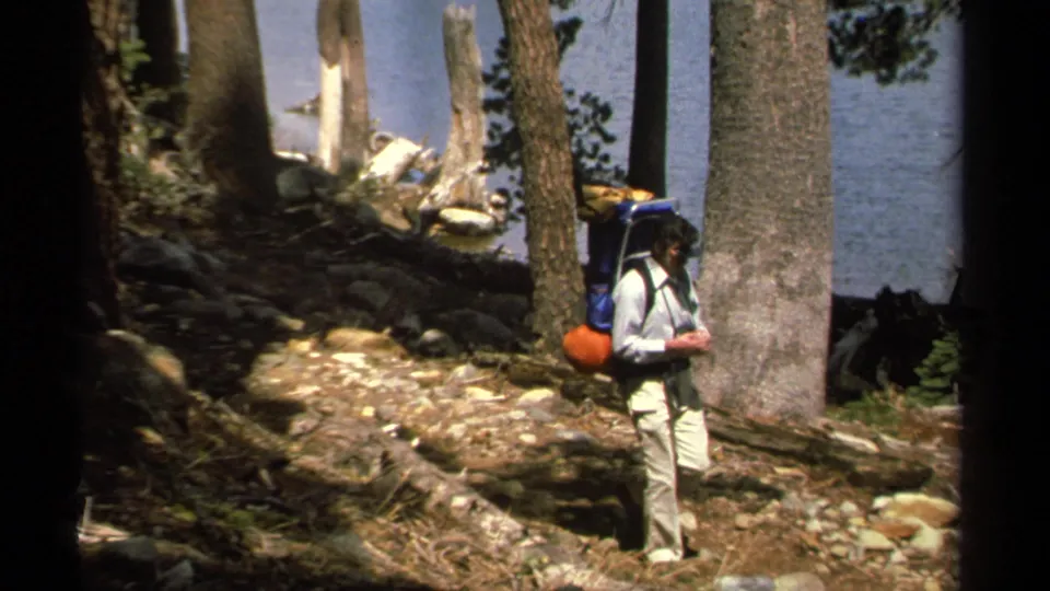 A backpacker in light clothing walks along the rocky Lake Tahoe forest trail as the second hiker has moved out of frame.