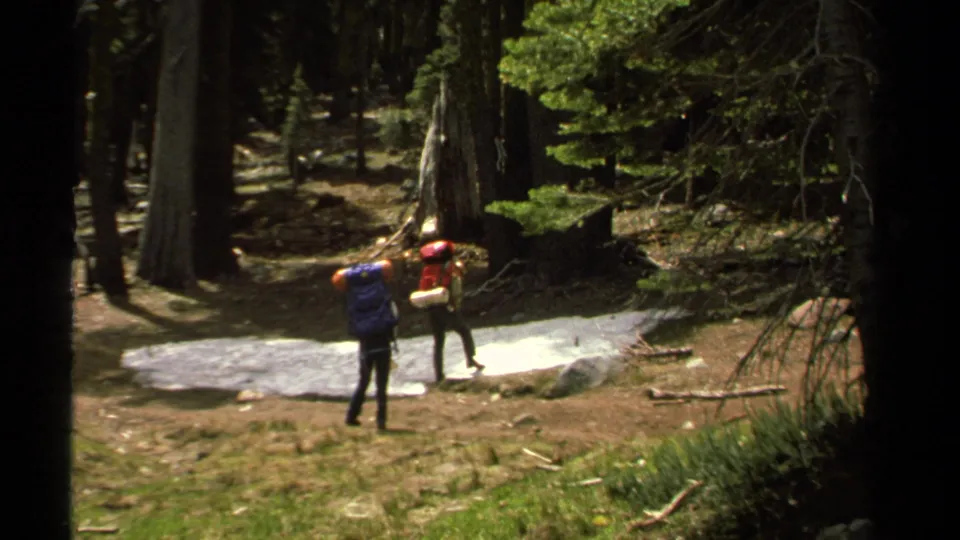 Two hikers with large packs pause in a 1978 Lake Tahoe forest, one closer to the camera and one near the pale path.