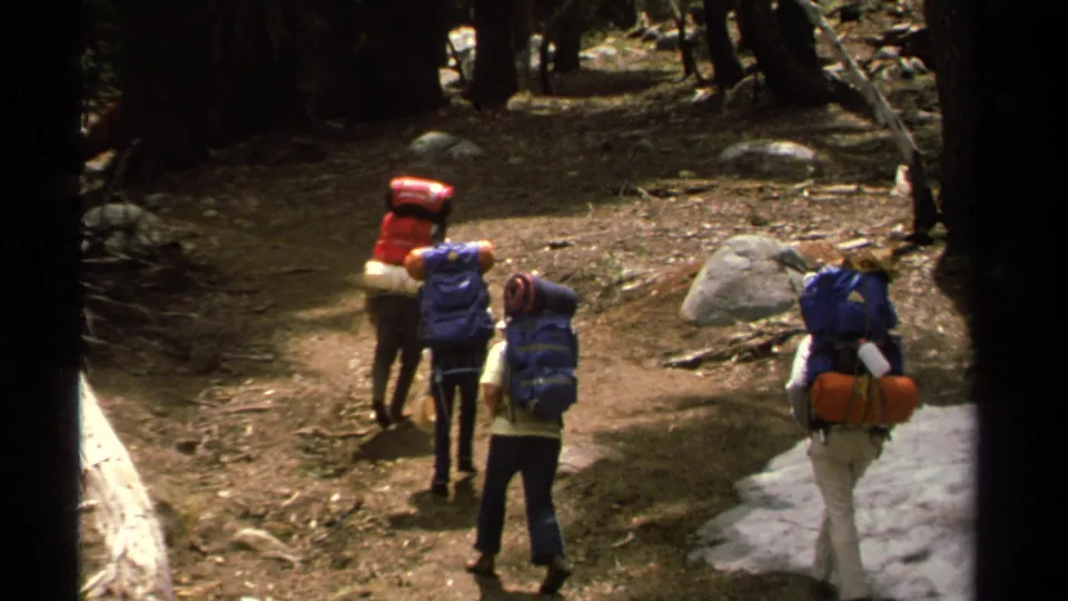 1978 Lake Tahoe home-movie frame showing hikers from behind as they continue along a wooded trail near lingering snow.