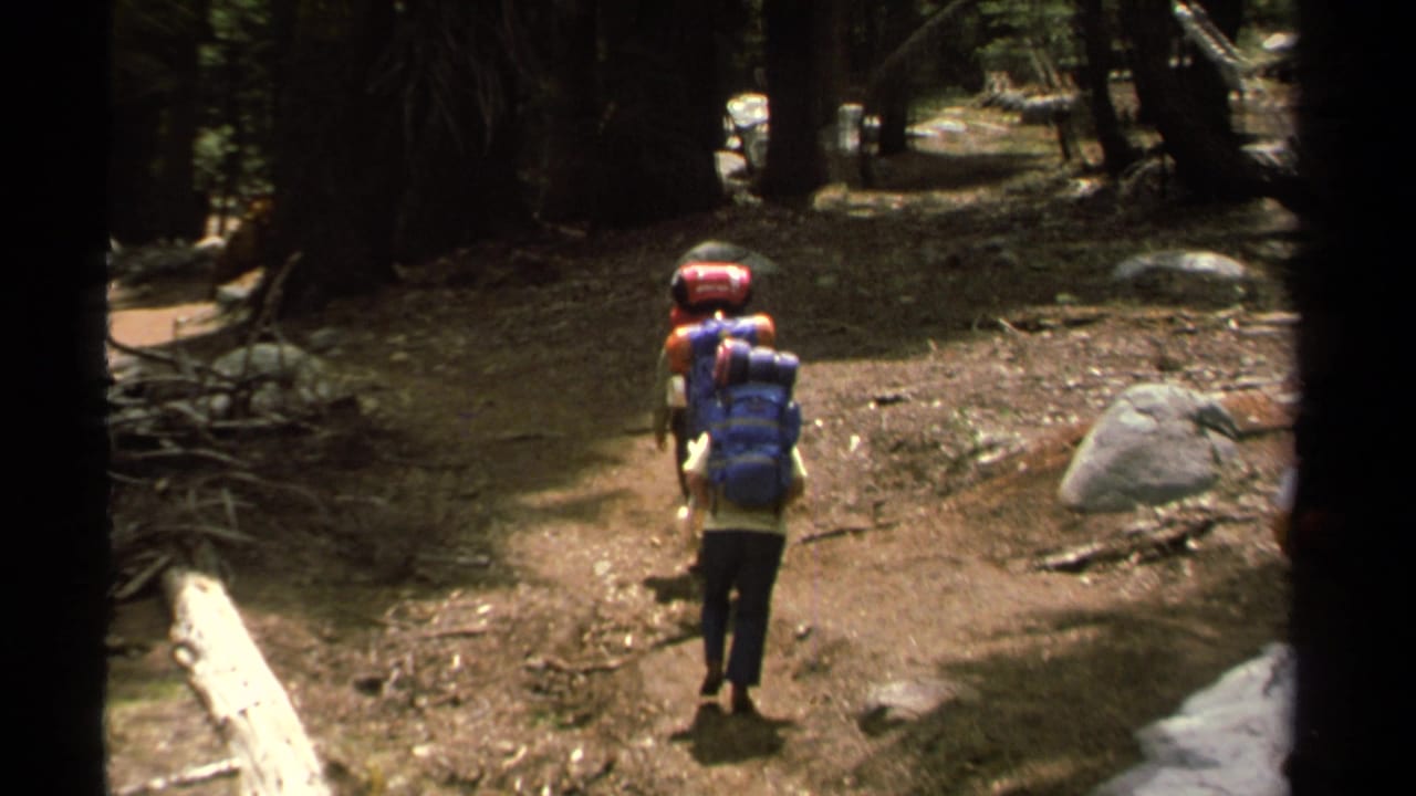 A single hiker carrying a red and blue backpack walks away on a Lake Tahoe forest path in 1978 archival 8mm footage.