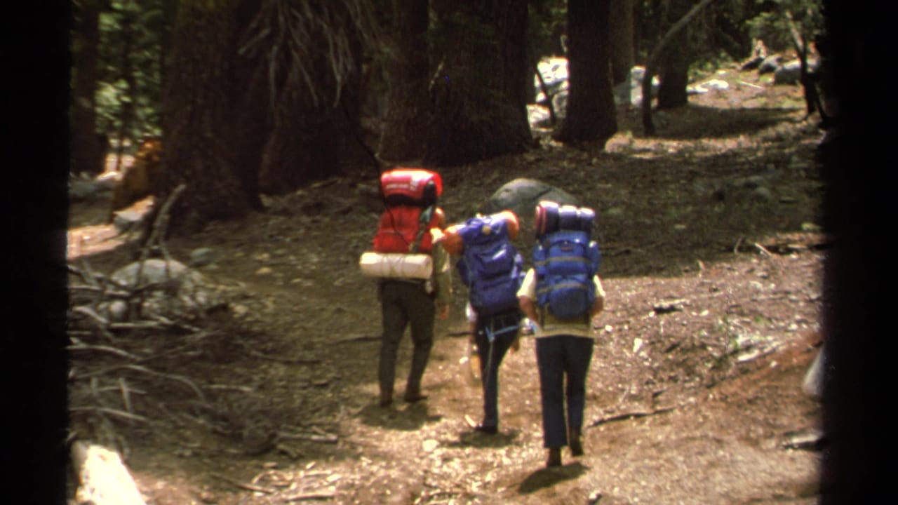 Three hikers with large packs move along a Lake Tahoe forest trail in 1978 home-movie footage.