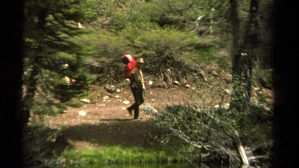 In the 1978 Lake Tahoe trail footage, a distant backpacker with a red pack moves through a wooded path.