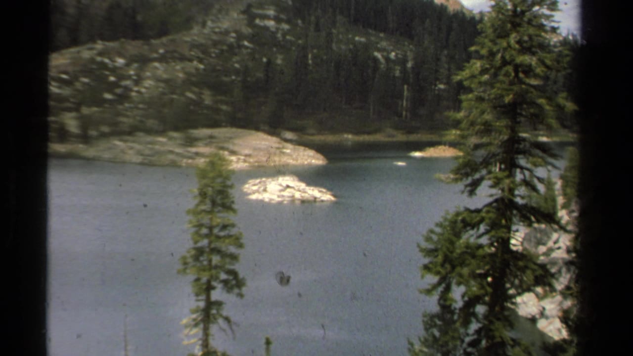 1978 Lake Tahoe home-movie frame showing a quiet mountain lake bordered by evergreen forest and granite shoreline.